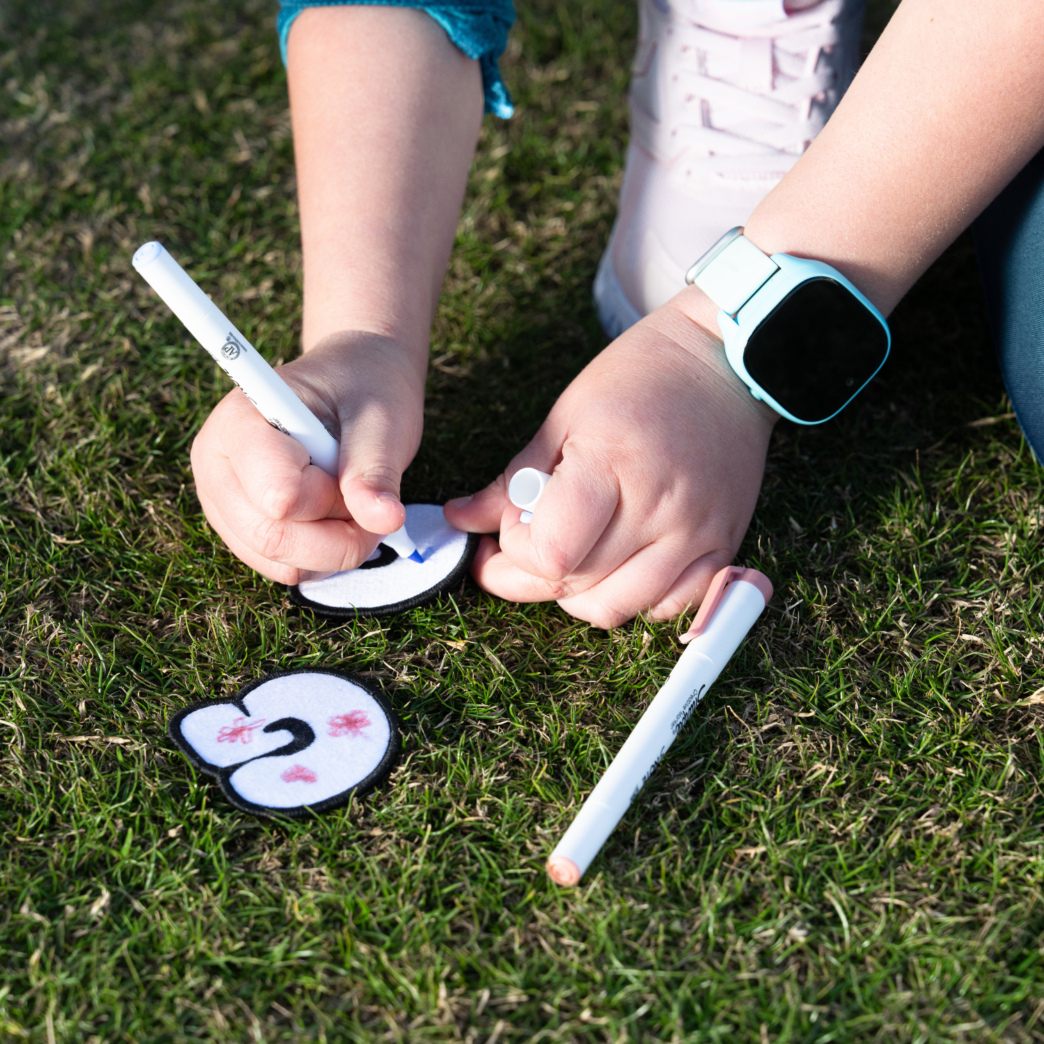 A child coloring a white embroidered letter patch with a blue and pink marker in the golf field