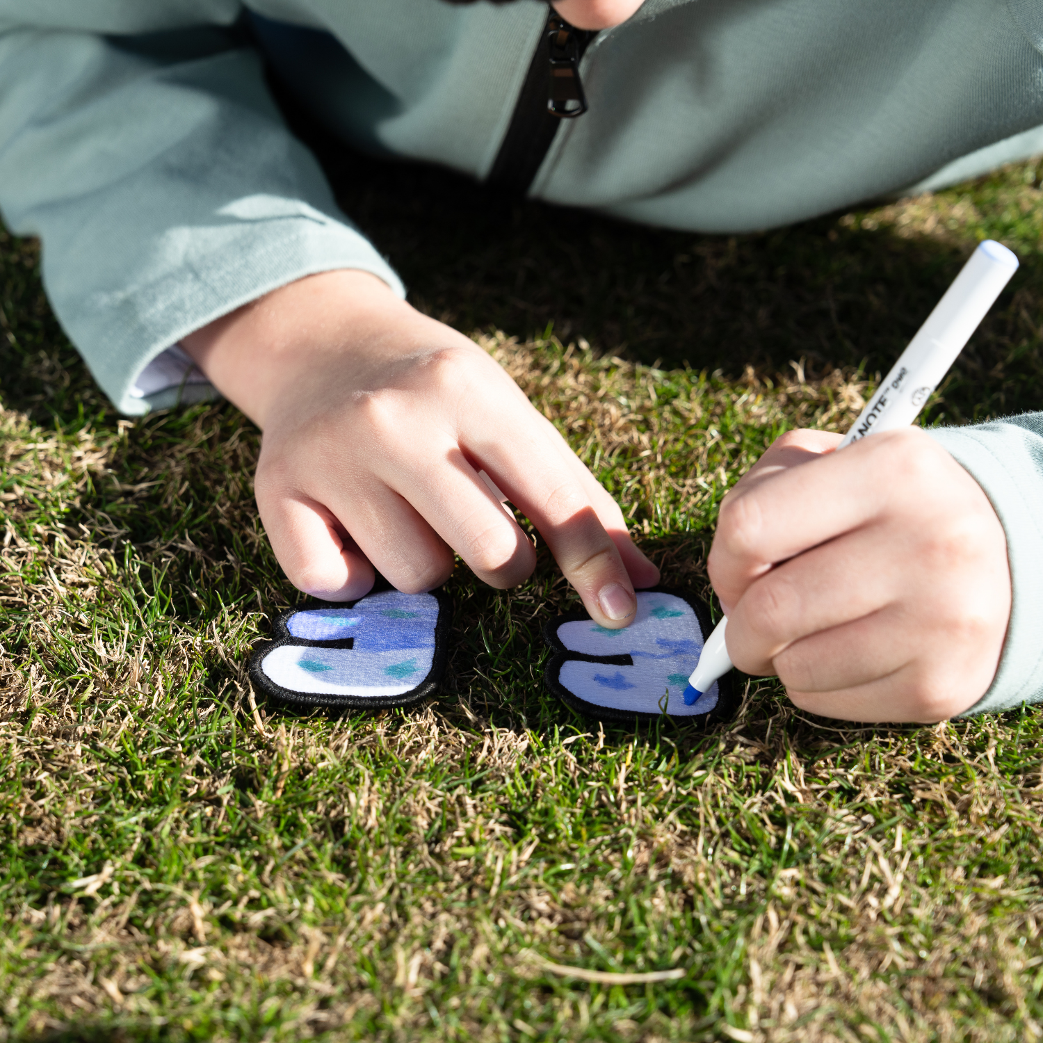 A child coloring a white embroidered letter patch with a blue and green marker in the golf field