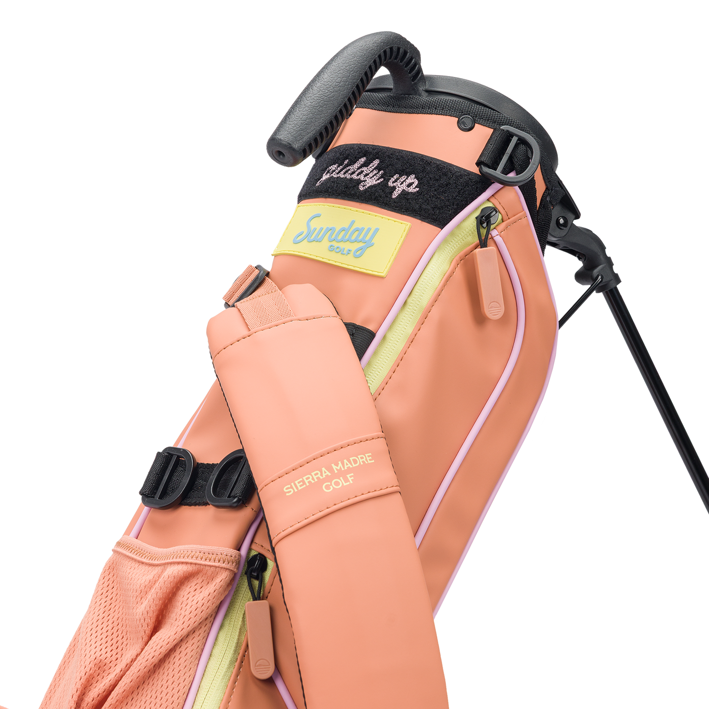 A close-up view of a Sunday Golf Loma bag in a peach colorway, featuring pastel accents. The bag has a "Sierra Madre Golf" label on the strap, a "Sunday Golf" logo patch on the side, and a "giddy up" embroidered message on the black velcro area near the top. The design includes multiple zippered pockets, mesh detailing, and a molded handle.