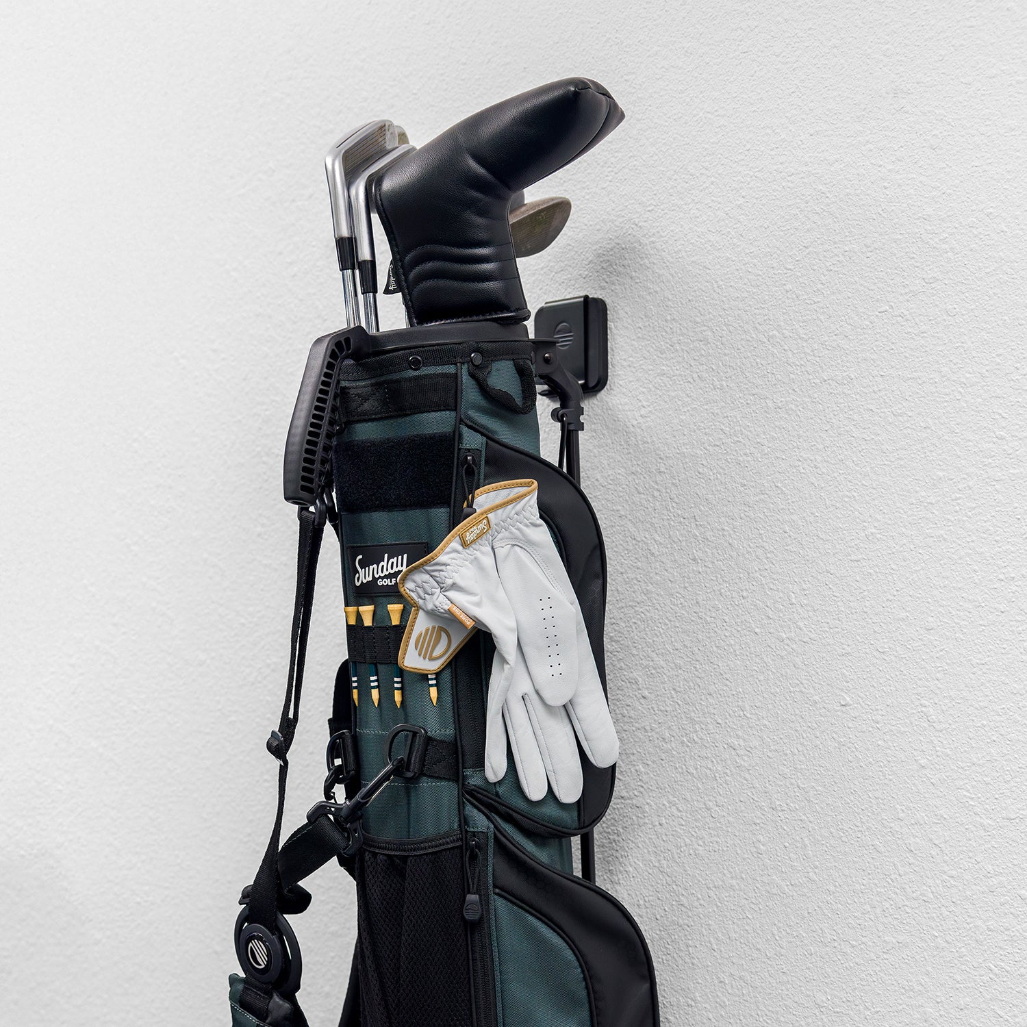 A black Loma Wall hook wall-mounted with the Loma bag with gloves, tees and clubs