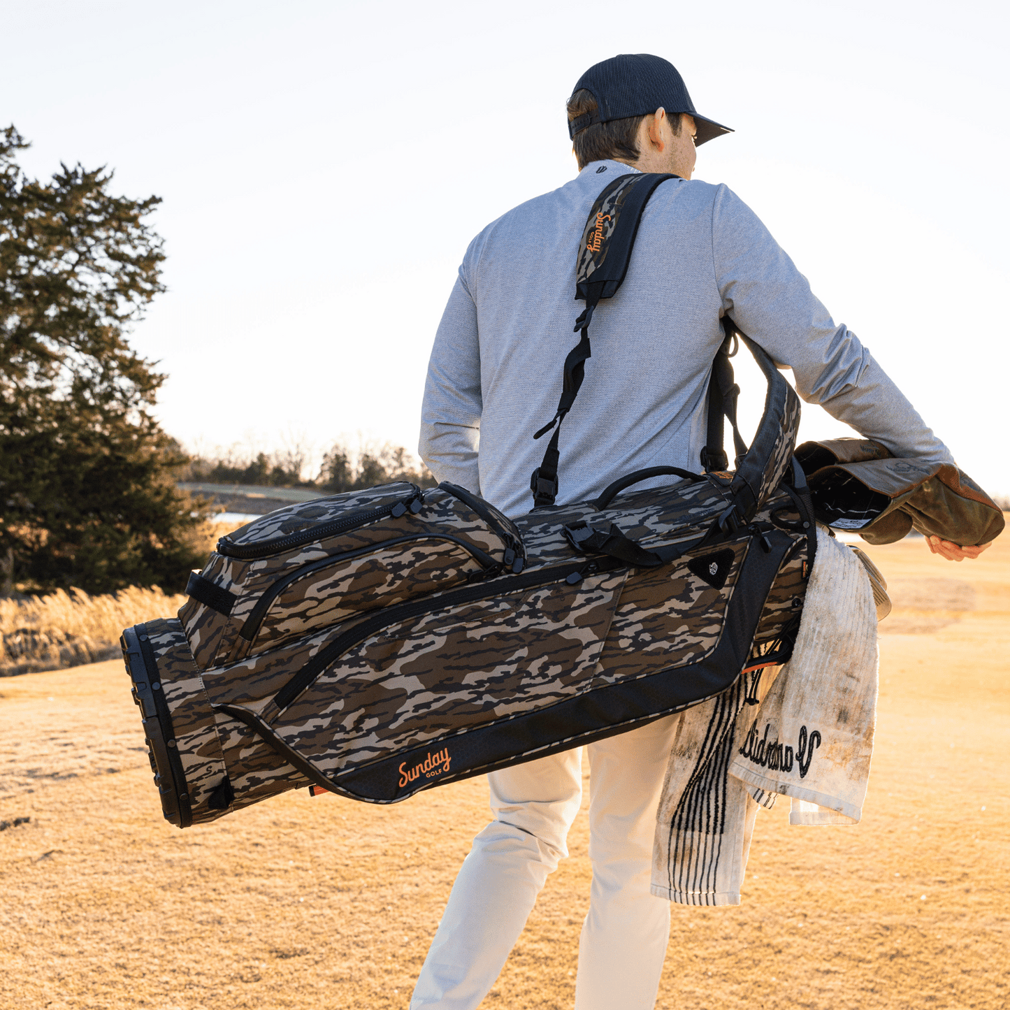 A man on the course carrying a Ryder golf bag in mossy oak bottomland on his side