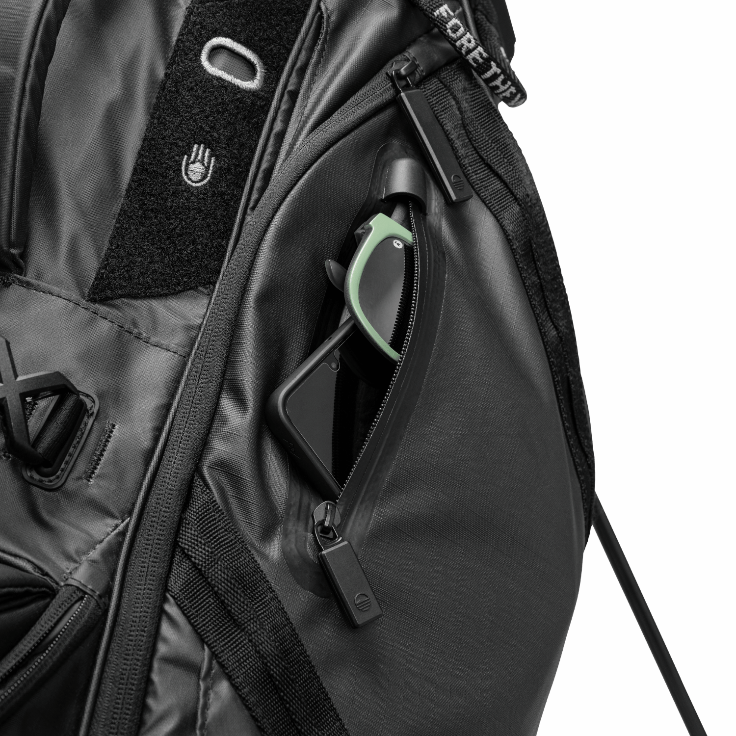 A close up shot of black Ranger golf bag's valuables pouch with a phone and sunglasses inside