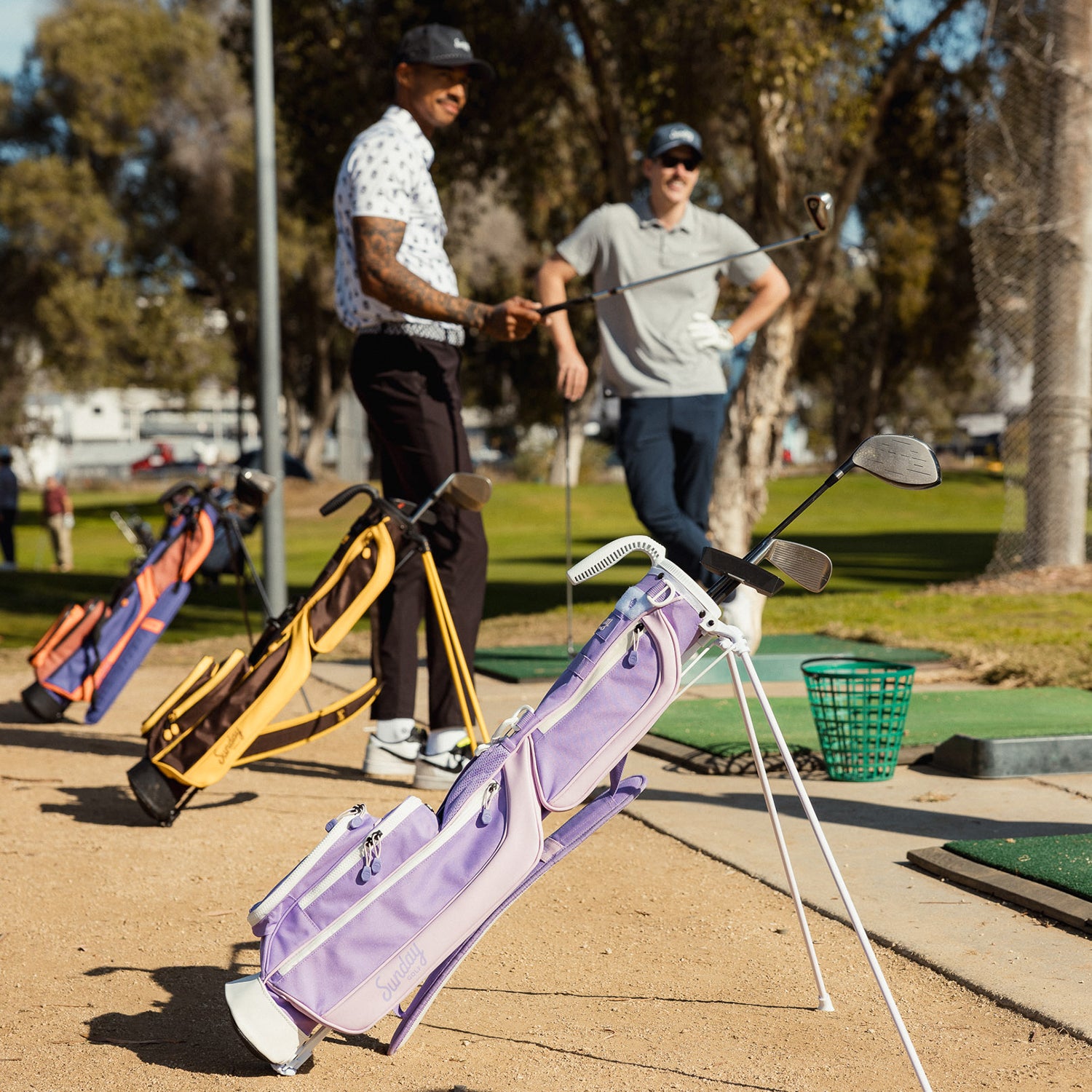 Two men standing at the driving range with a couple of Loma golf bags standing beside them