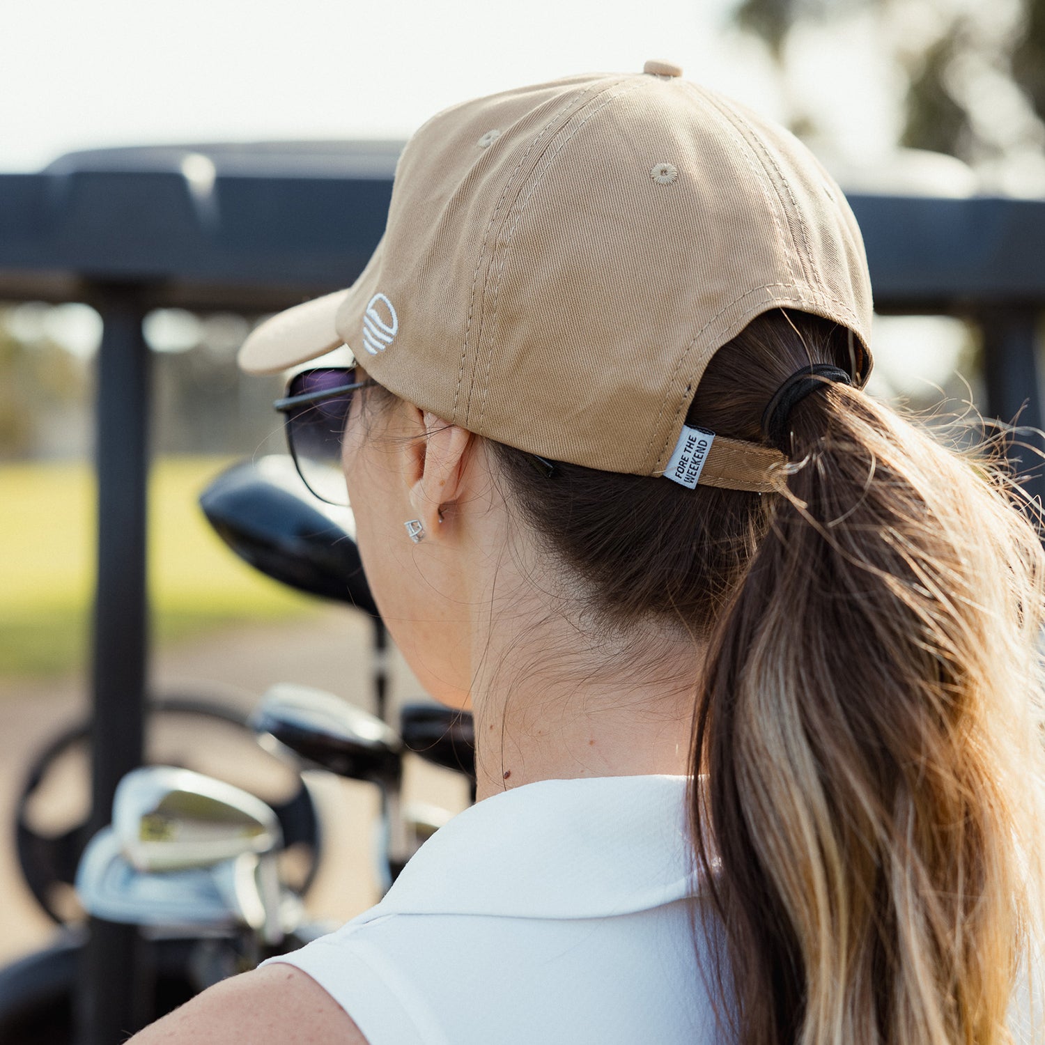 Back view of a woman wearing khaki dad golf hat with her hair tied into a ponytail