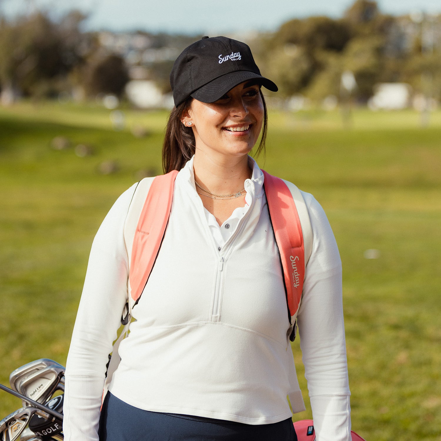 A woman wearing a matte black dad golf hat and a double strap golf bag