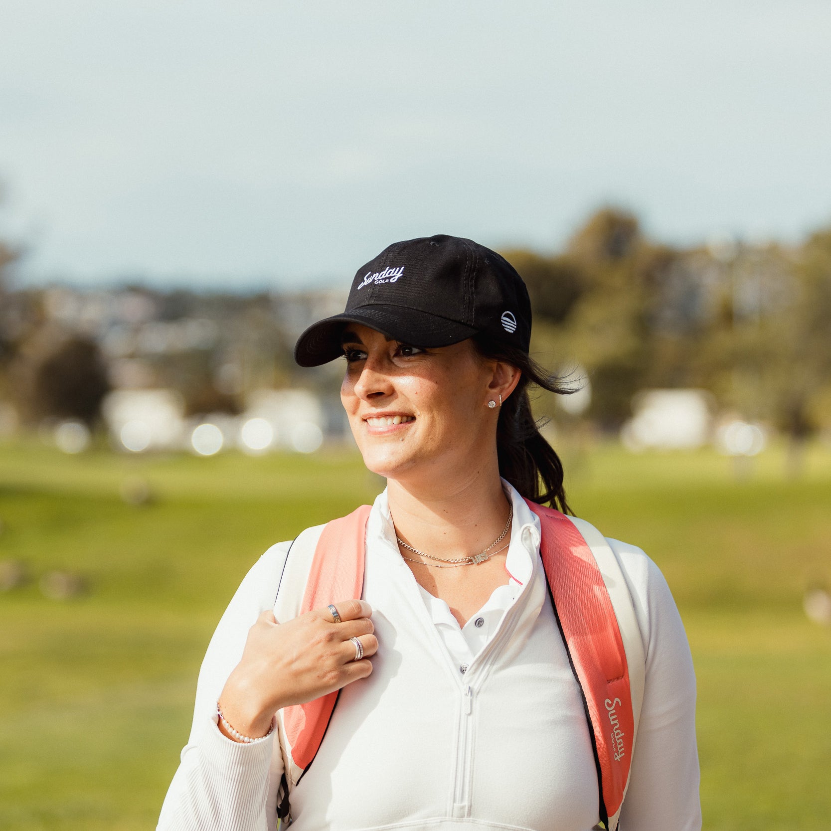 A woman wearing a matte black dad golf hat and a double strap golf bag