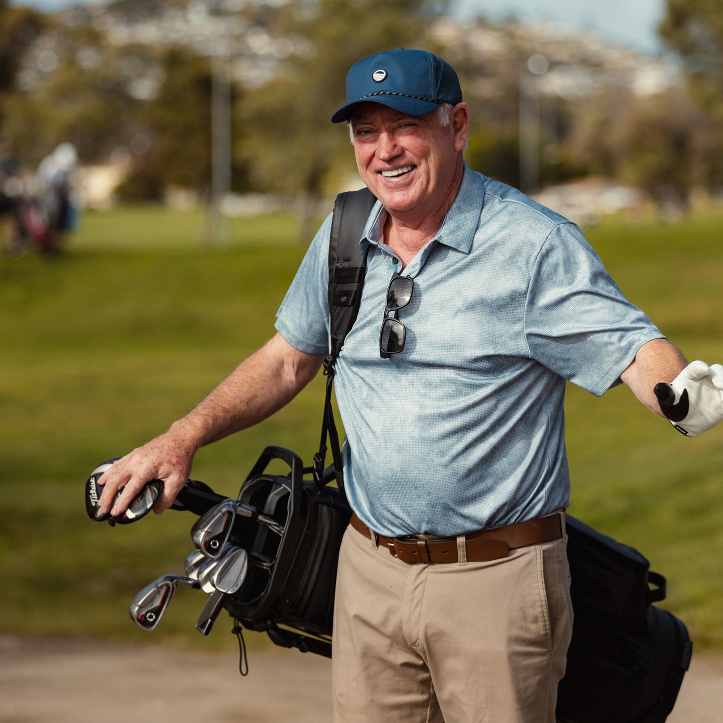 A man smiling while wearing navy Porter Lite golf hat and holding his golf clubs in his carry golf bag
