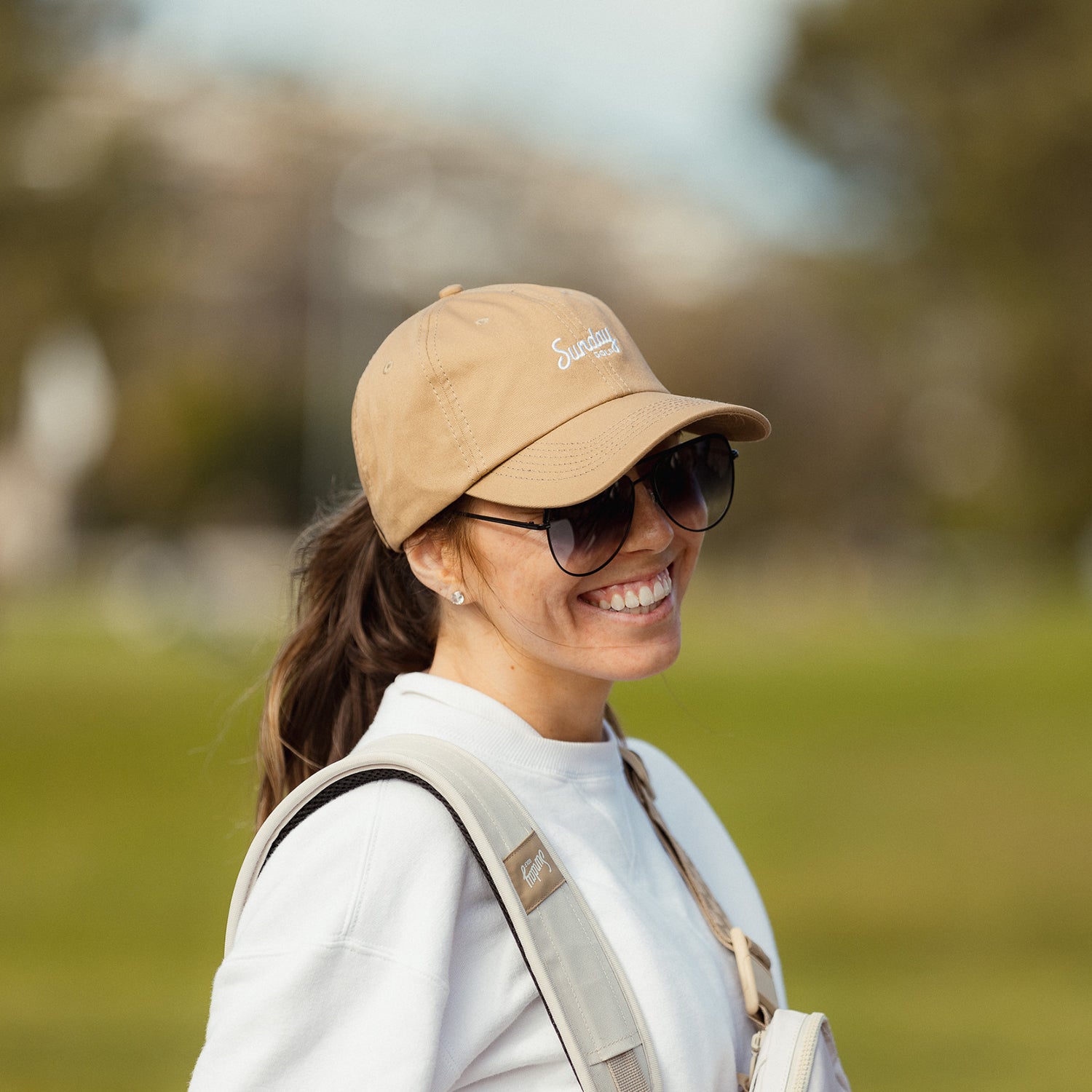 A woman smiling while wearing khaki dad golf hat and sunglasses
