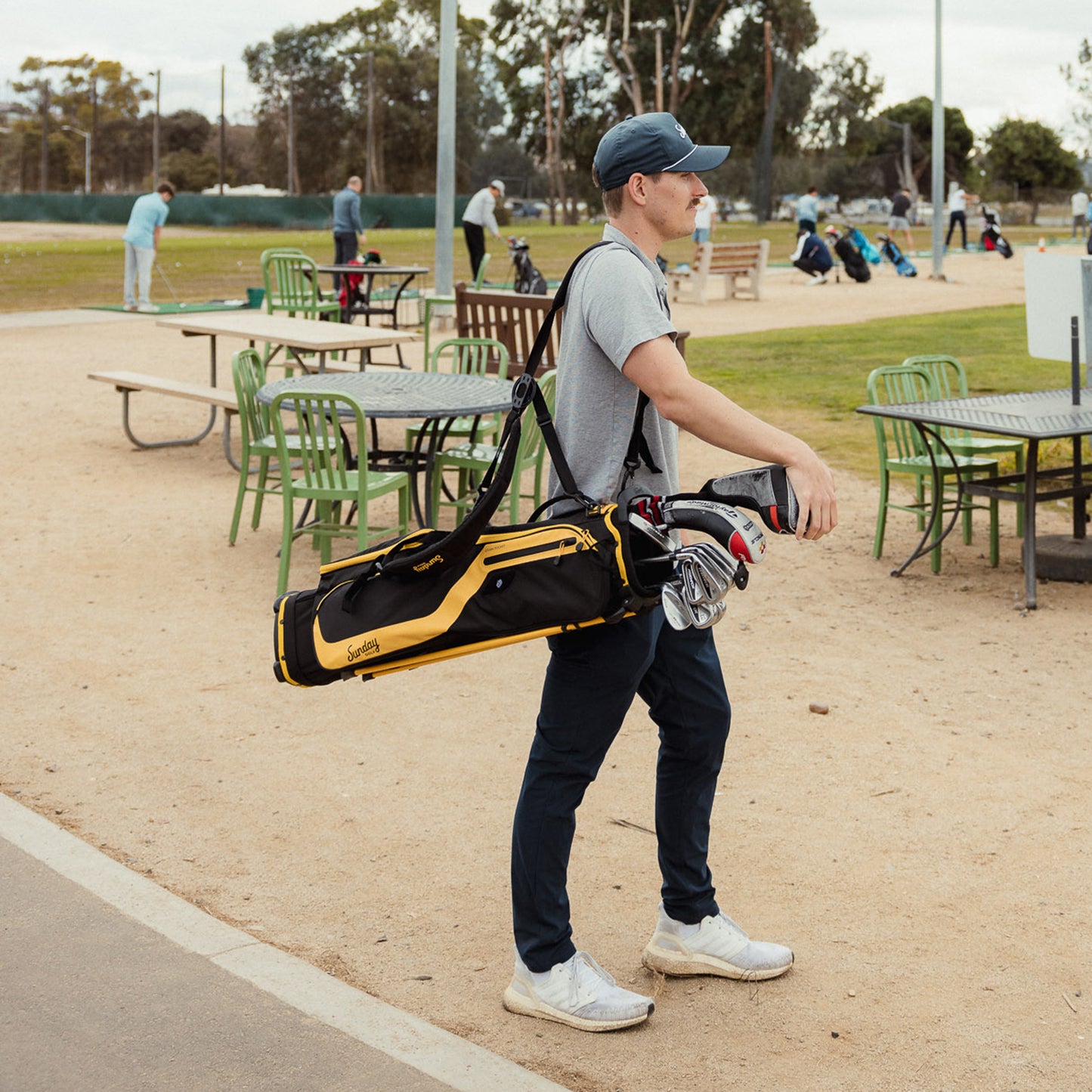 A guy wearing a navy blue golf hat walking on the course while carrying an El Camino golf bag in black and yellow