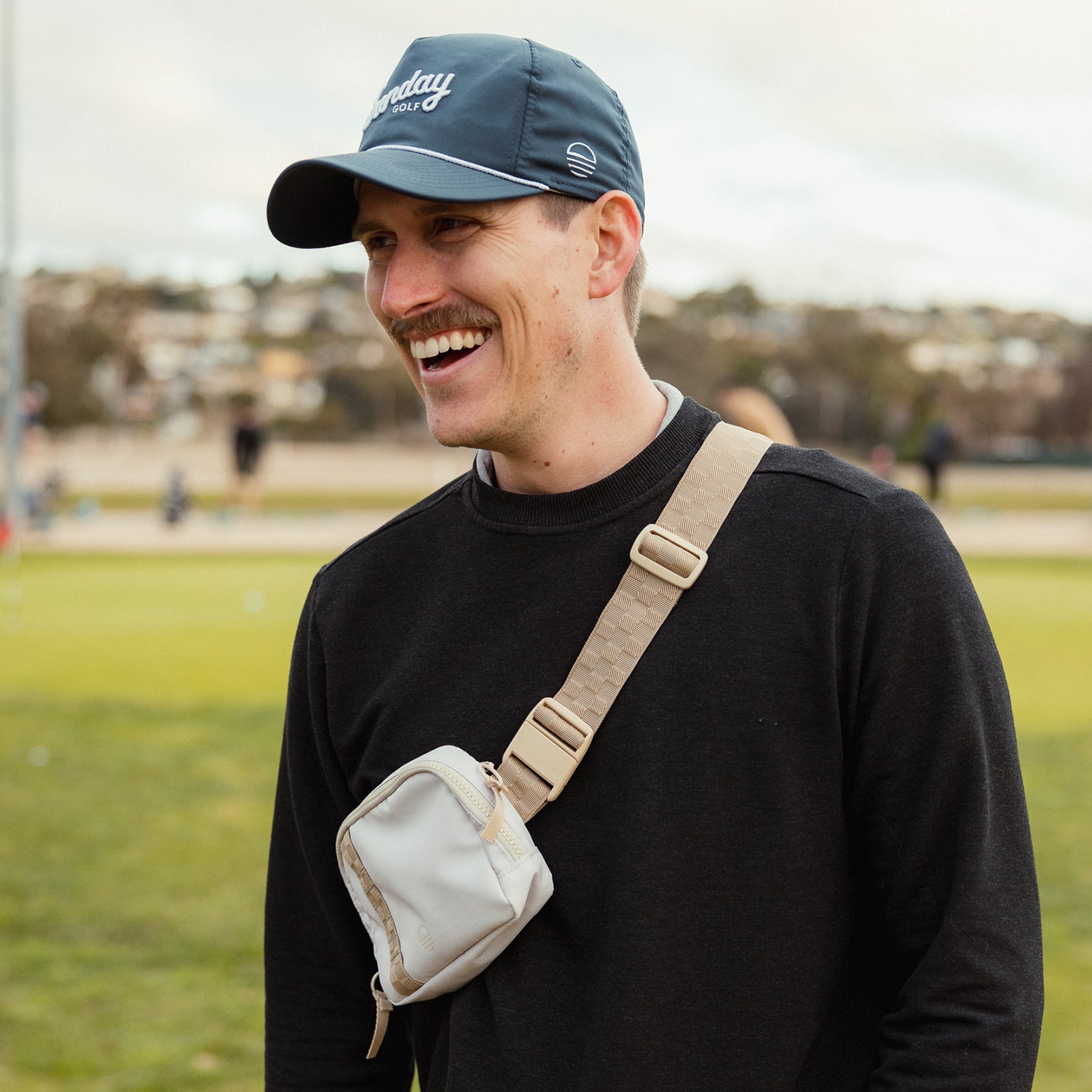 A man wearing a toasted almond belt bag and a golf hat