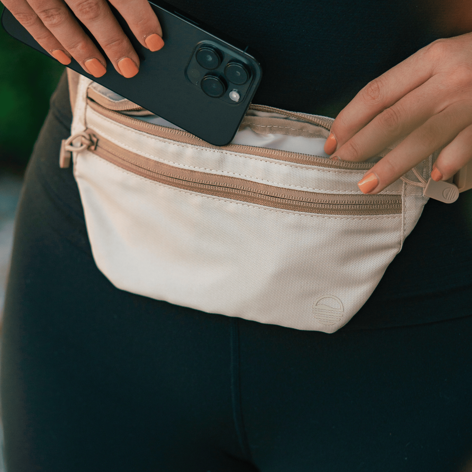 Toasted Almond Runner Sling worn by a woman as she places her phone inside