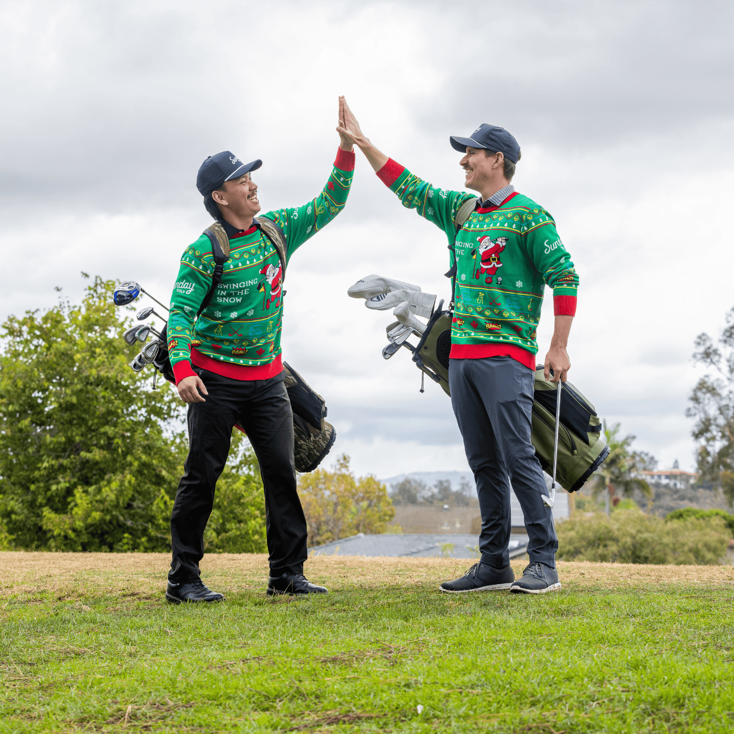 Two golfers in matching Ugly Sweaters  giving a high-five on a golf course.