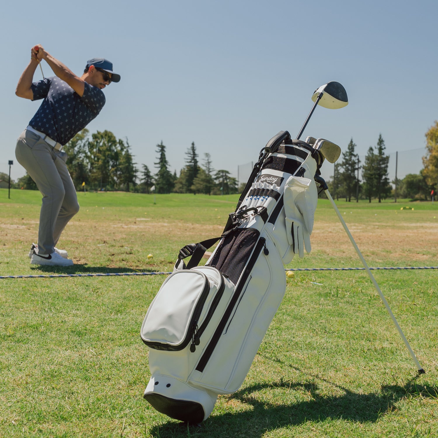 A full front shot on the course of standing Loma XL S-Class golf bag in white vegan leather with a man playing in the background