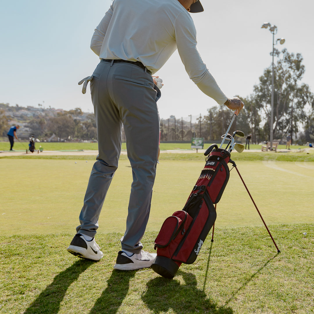 A man on the golf course putting a golf club in his ron burgundy Loma golf bag