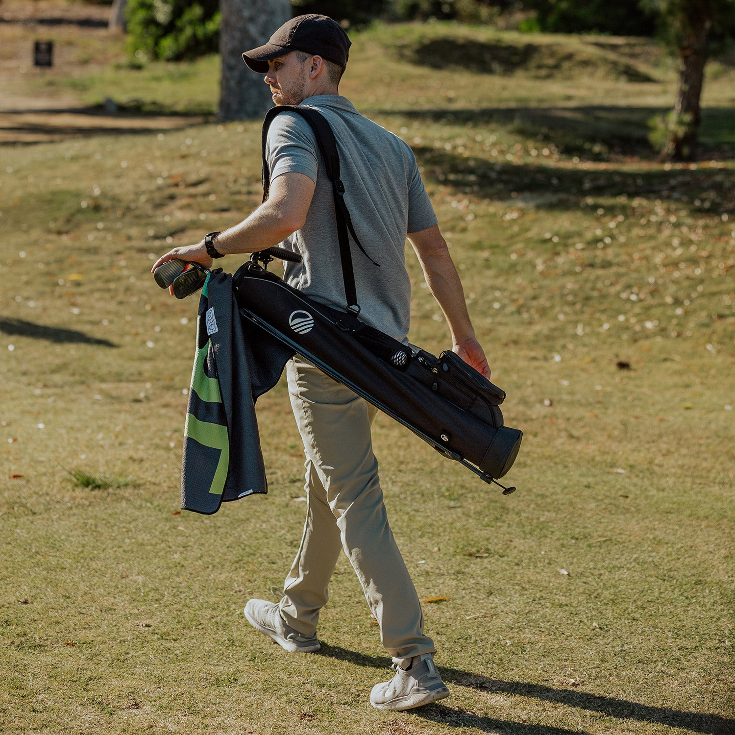 A man carrying a matte black Loma golf bag while walking on the course