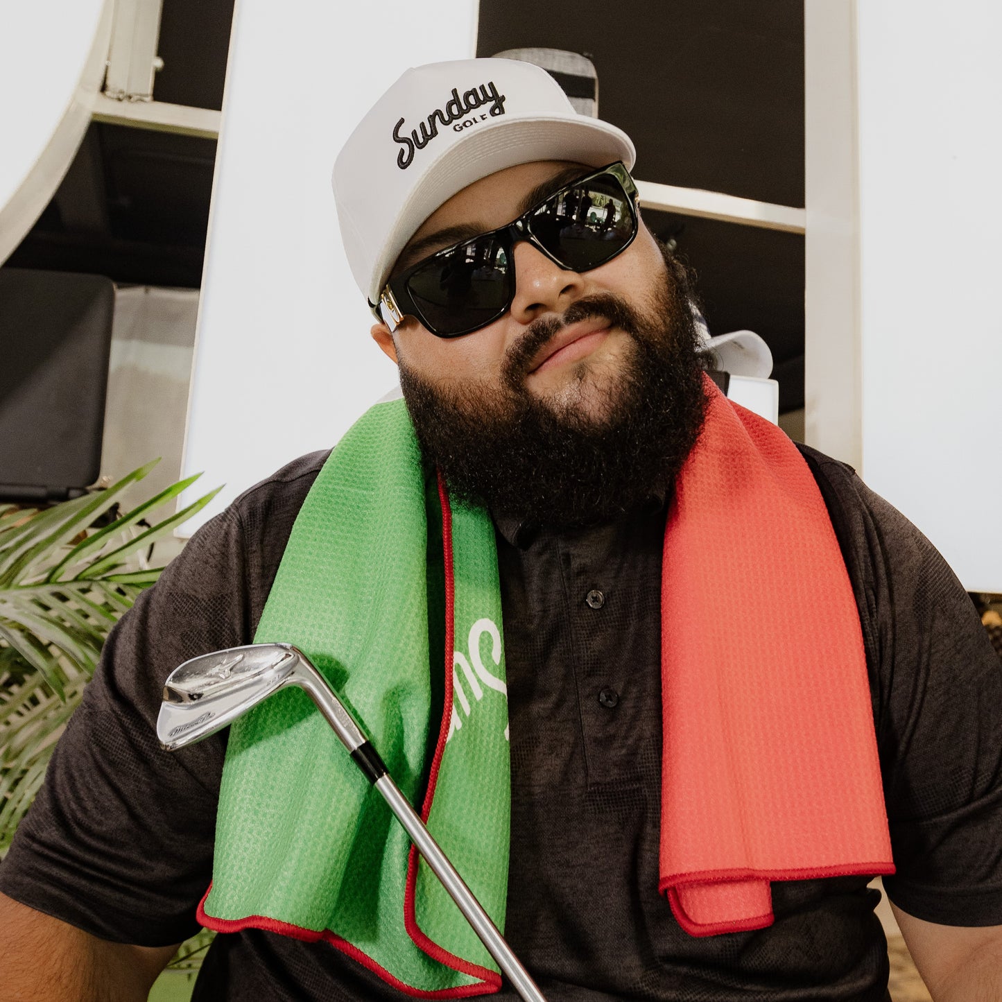 A man wearing white and black rope golf hat with a golf towel around his neck