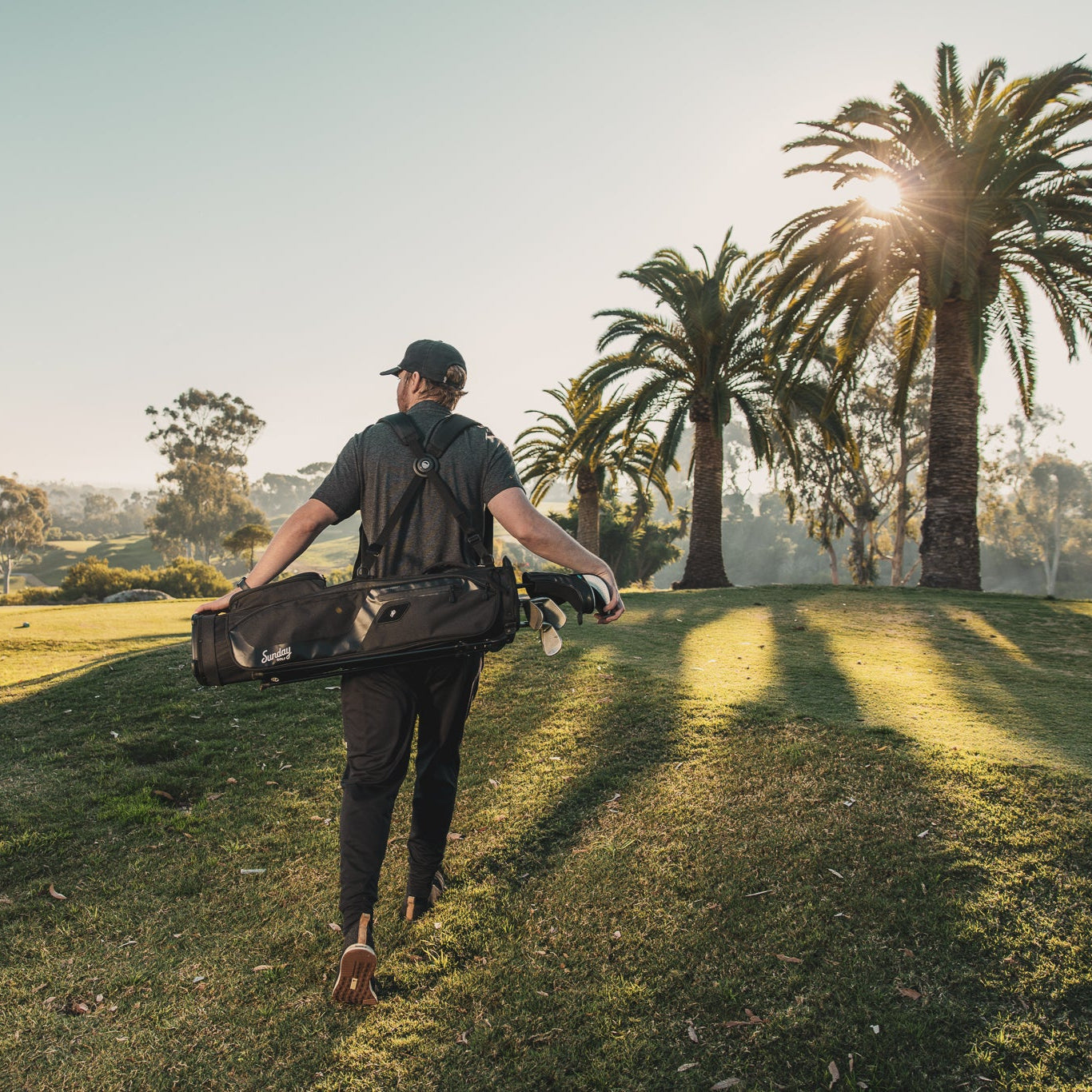 man carrying the matte black El Camino golf bag by Sunday golf on golf course with palm trees