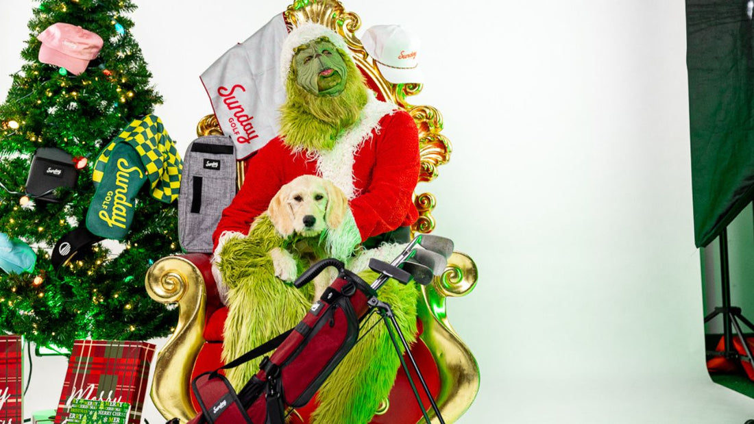 The Grinch dressed as Santa holds a puppy, surrounded by Sunday Golf bags and accessories