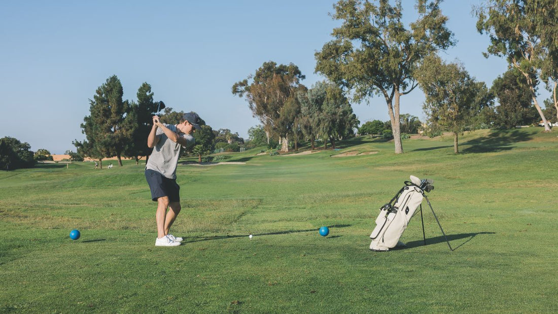 man in a gray shirt swings a golf club on a sunny course, with a Sunday Golf Loma golf bag 