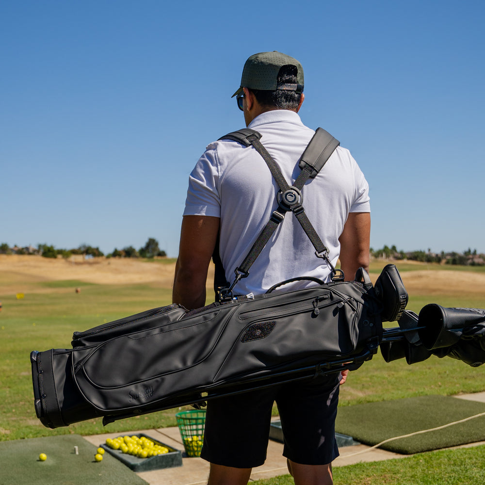 A man standing on the course facing backward showing off an El Camino S-Class golf bag in black vegan leather material with a double strap