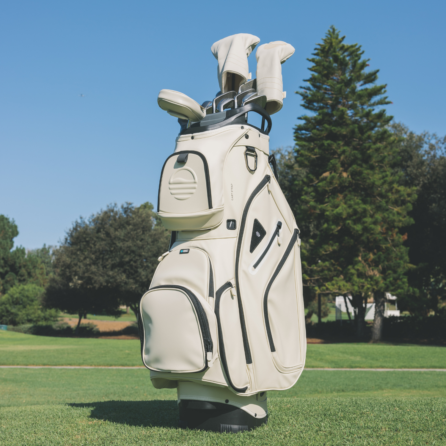 Big Rig S-class golf bag in Cream with clubs on a grassy field with trees in the background