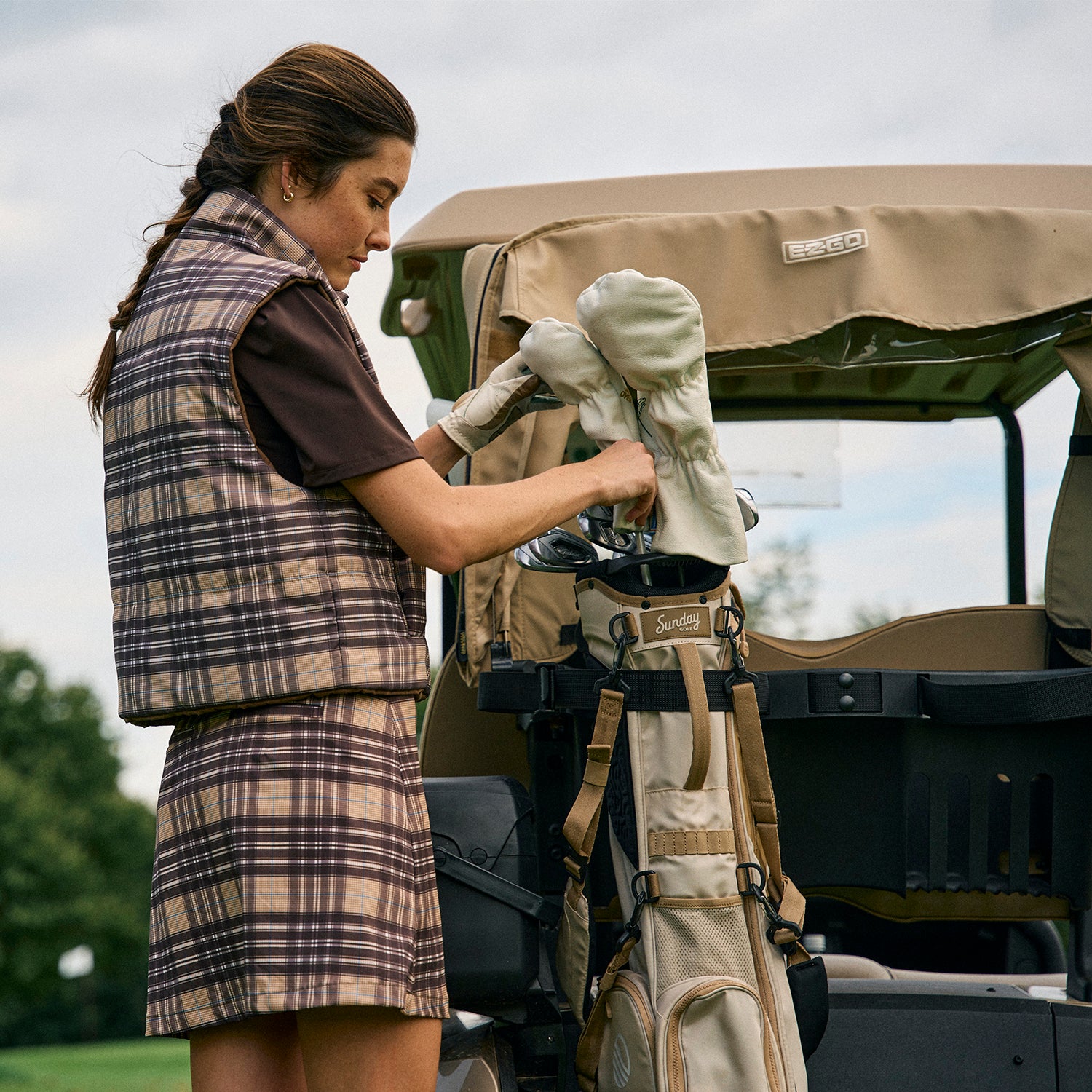 A woman beside a golf cart organizing her clubs in the El Camino golf bag in toasted almond