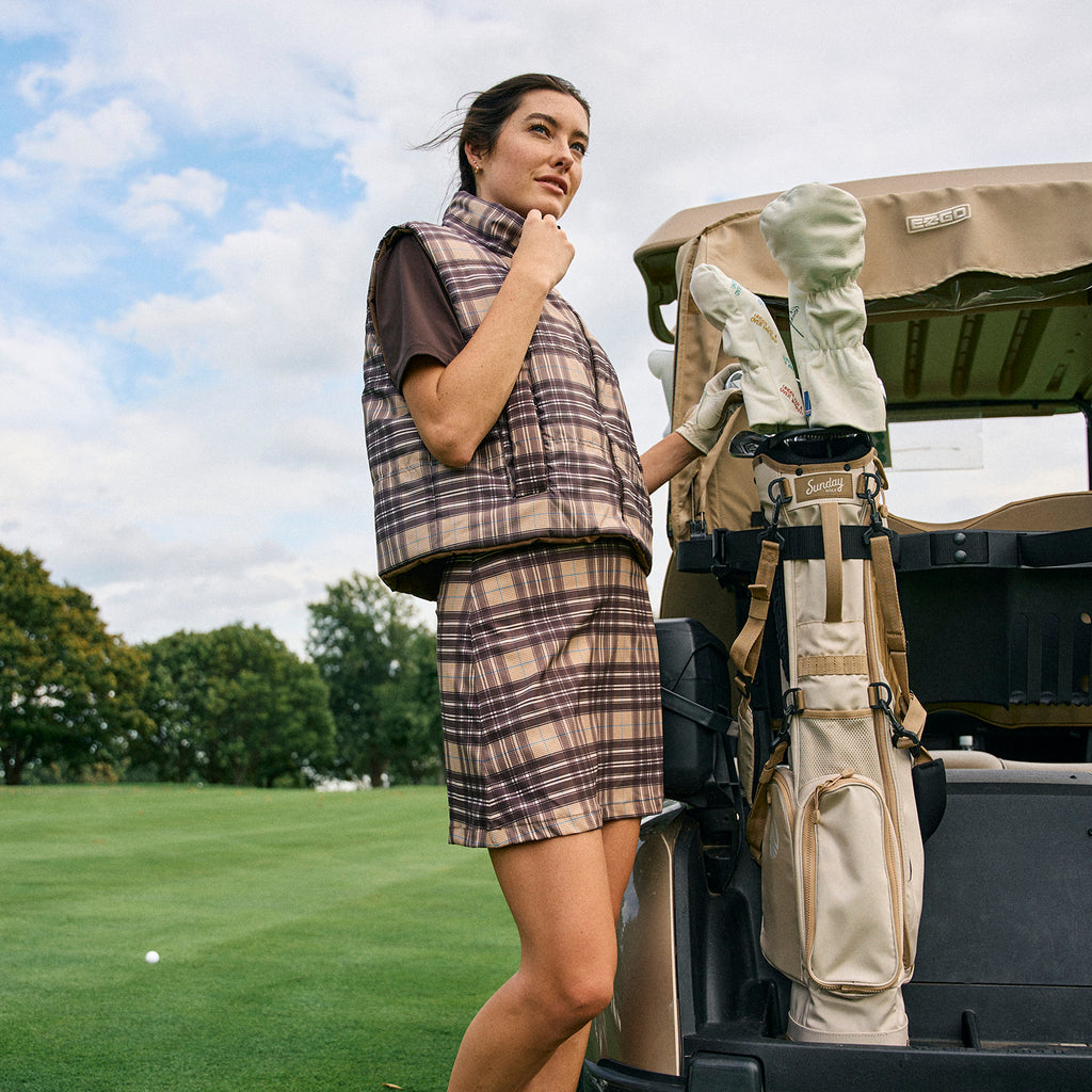 A woman standing beside a golf cart bag containing the El Camino golf bag in toasted almond