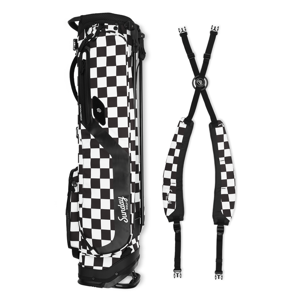 A full shot of El Camino golf bag in Black/White Checker laying flat sideways beside its double strap 
