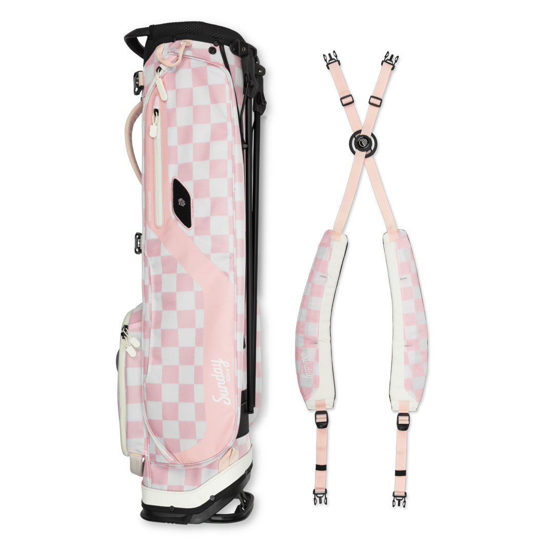 A full shot of El Camino golf bag in Pink/White Checker laying flat sideways beside its double strap 
