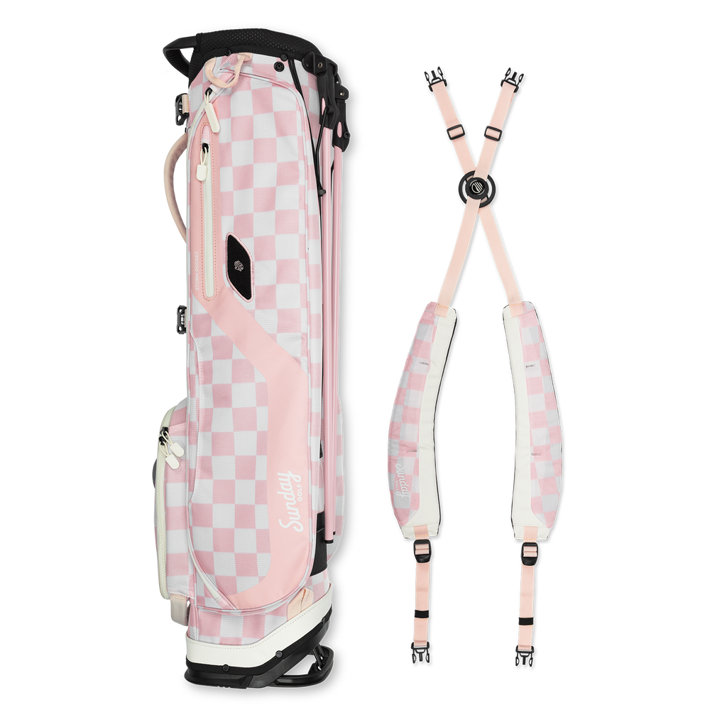 A full shot of El Camino golf bag in Pink/White Checker laying flat sideways beside its double strap 

