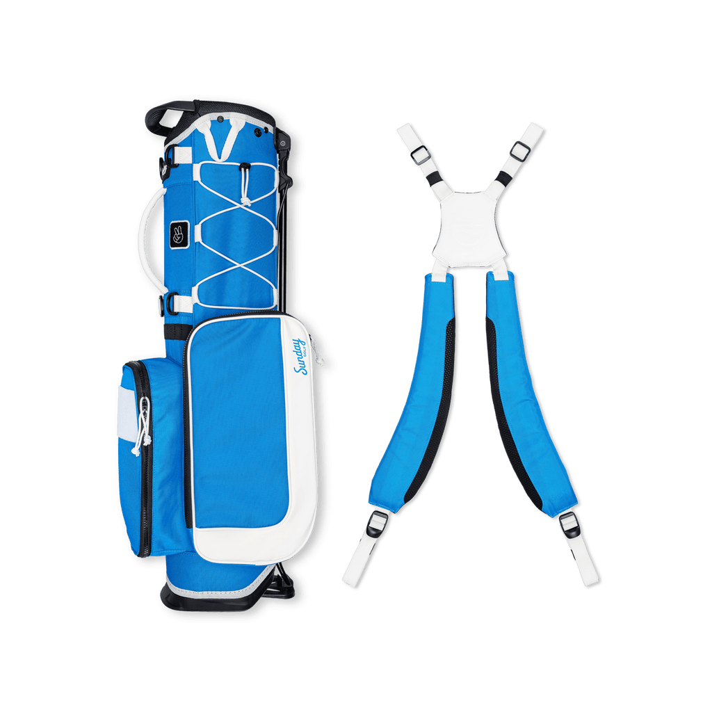 A full shot of a blue & white Recess kids golf bag laying flat sideways beside its double straps

