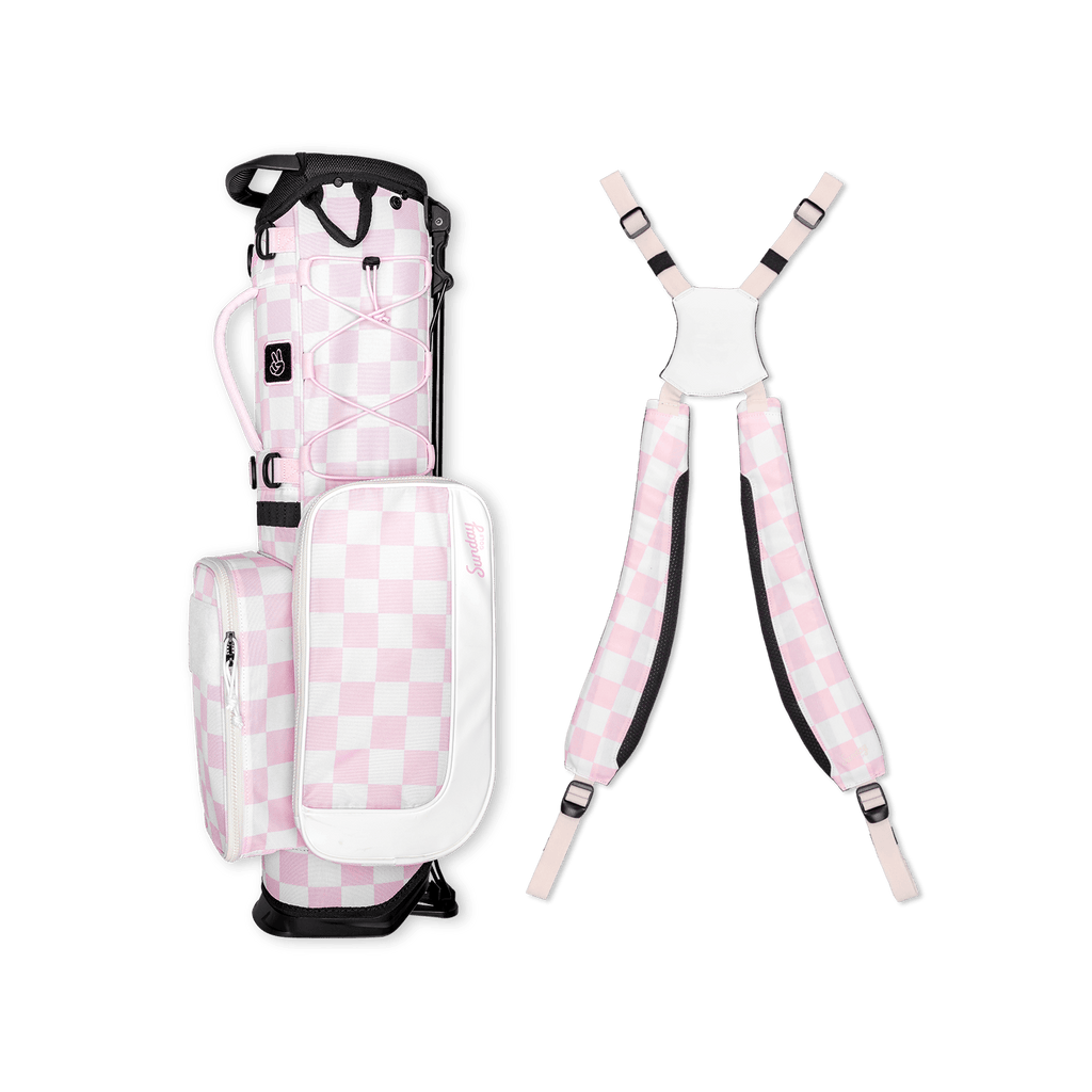 A full shot of a checkered Pink & White Recess kids golf bag laying flat sideways beside its double straps
