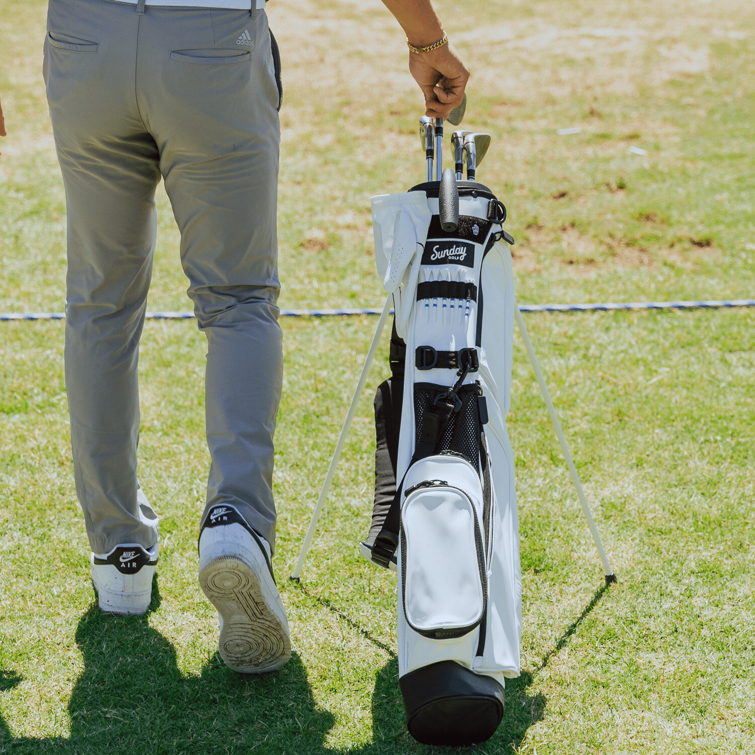 A man standing on the course beside a Loma S-Class golf bag in white vegan leather