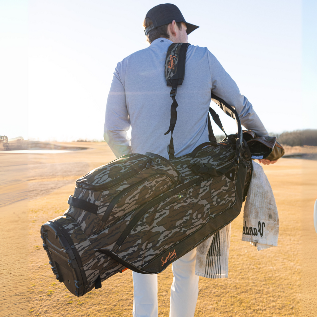 A man on the course carrying a Big Rig golf bag in mossy oak bottomland on his back