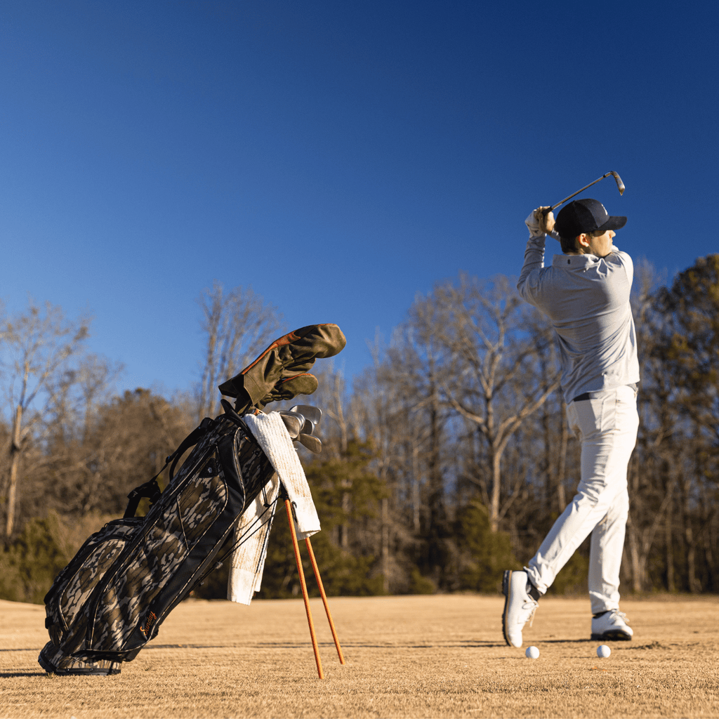 A man playing on the course while his Ryder golf bag in mossy oak bottomland is standing behind him