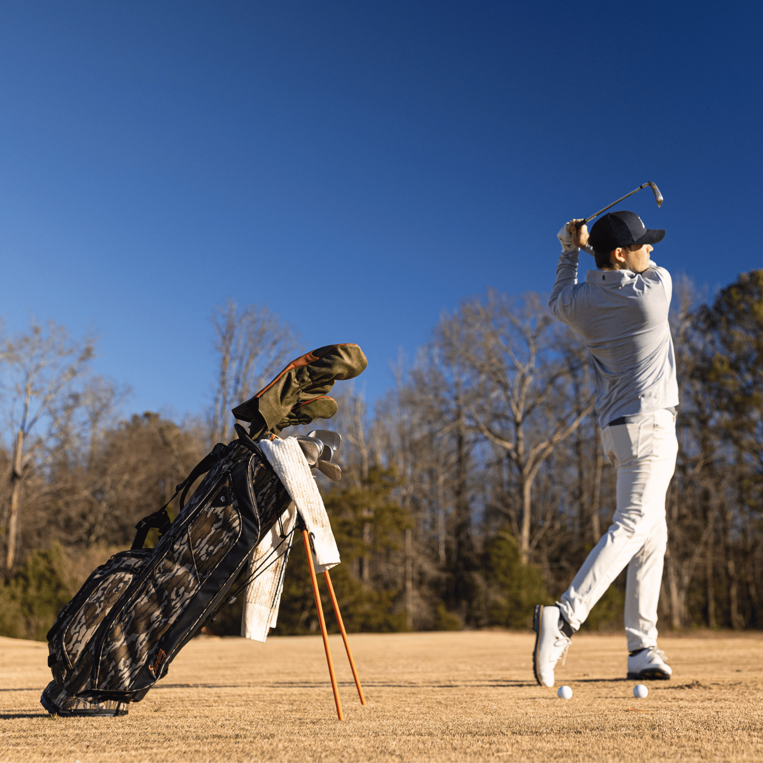 A man playing on the course while his Ryder golf bag in mossy oak bottomland is standing behind him