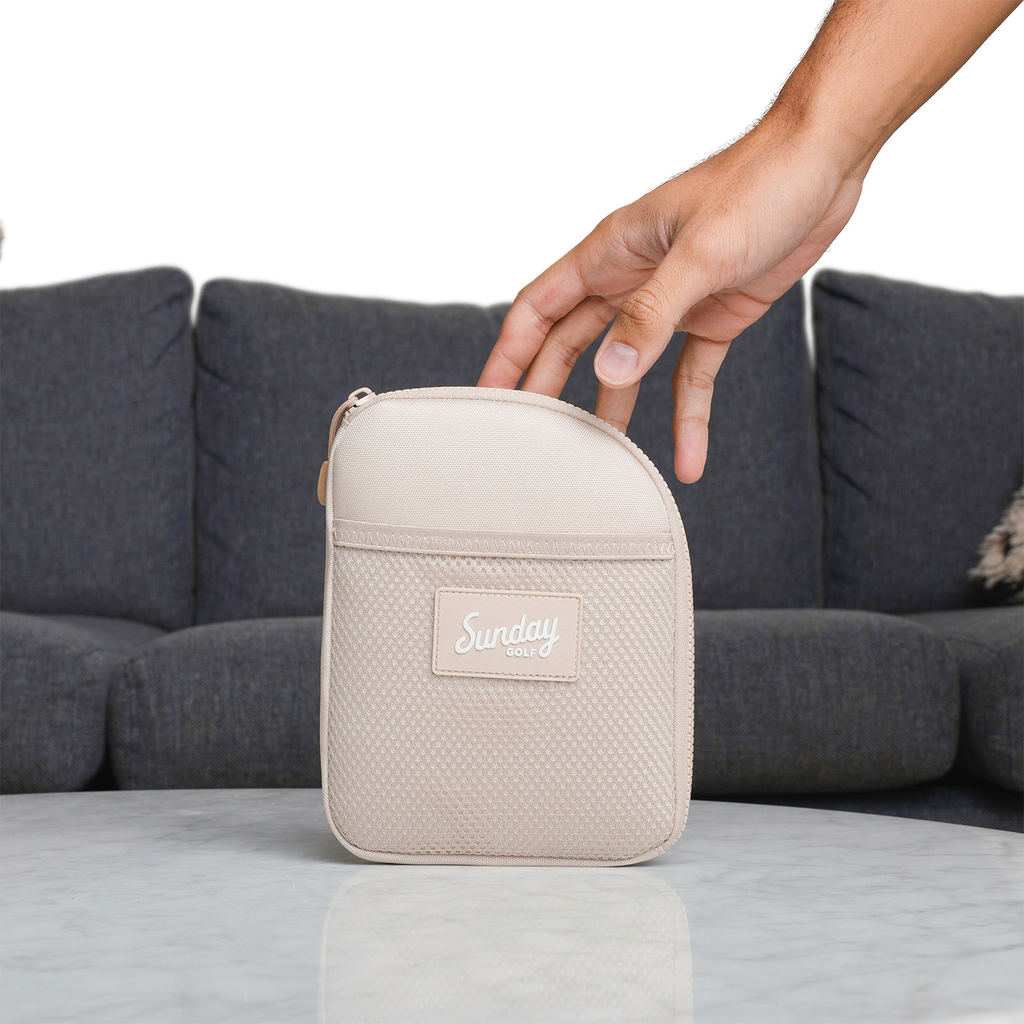 A hand about to grab a toasted almond nickel bag valuables pouch from a table