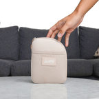 A hand about to grab a toasted almond nickel bag valuables pouch from a table