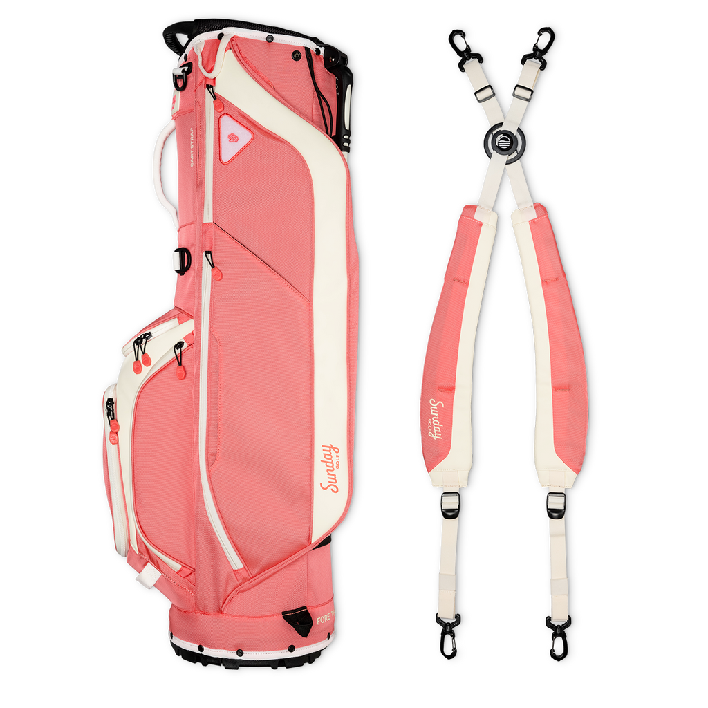 A full shot of Ryder golf bag in coral laying flat sideways beside its double strap