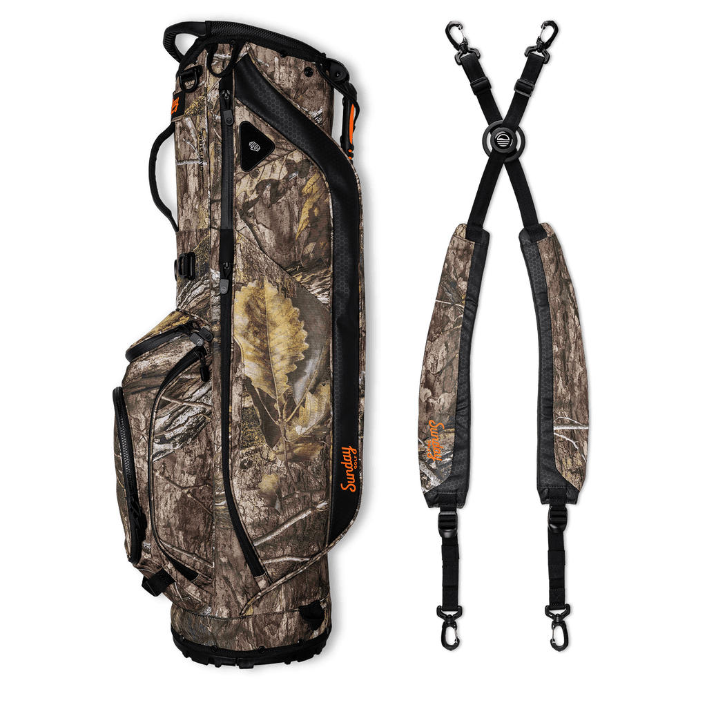 A full shot of Ryder golf bag in mossy oak country dna laying flat sideways beside its double strap