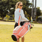 A woman carrying a Ryder golf bag in coral on her side