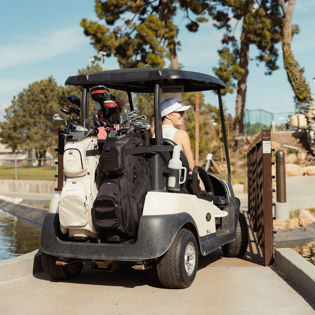 Big Rig golf bags in toasted almond and matte black at the back of a golf cart with two passengers