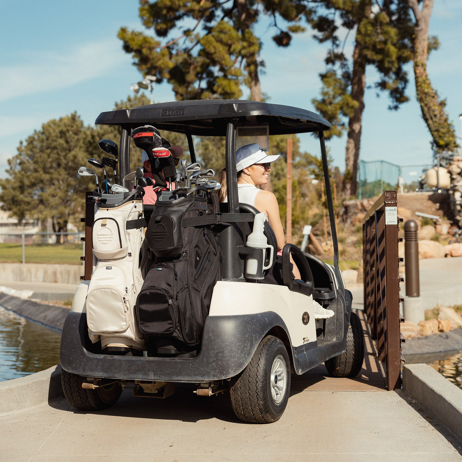 Big Rig golf bags in toasted almond and matte black at the back of a golf cart with two passengers