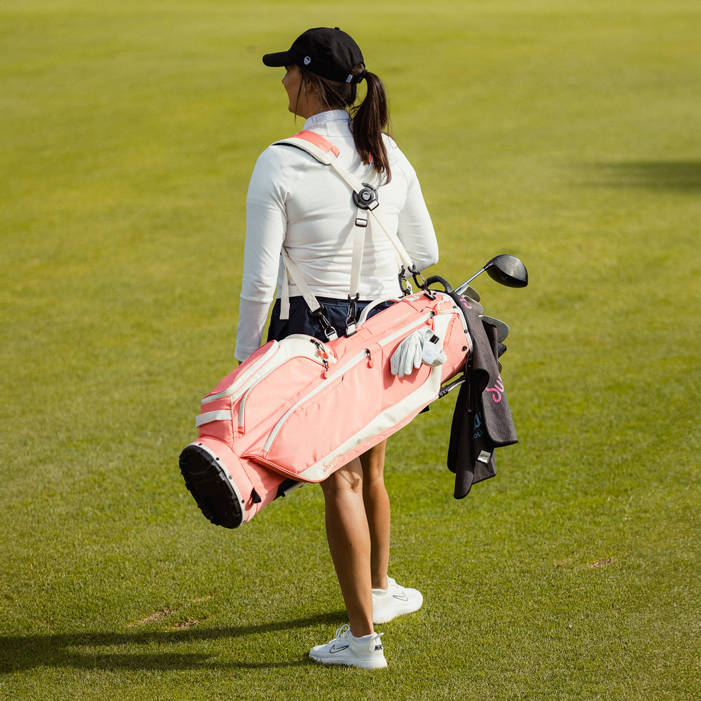 A woman carrying a Ryder golf bag in coral on her back using its double strap