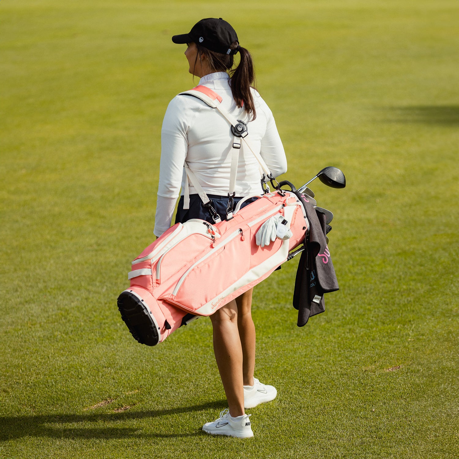 A woman carrying a Ryder golf bag in coral on her back using its double strap
