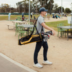 A guy wearing a navy blue golf hat walking on the course while carrying an El Camino golf bag in black and yellow 