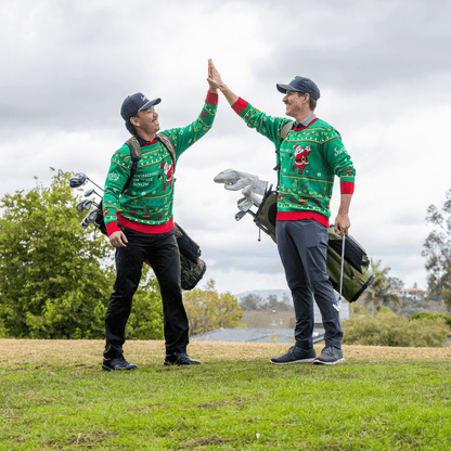 Two golfers in matching Ugly Sweaters  giving a high-five on a golf course.