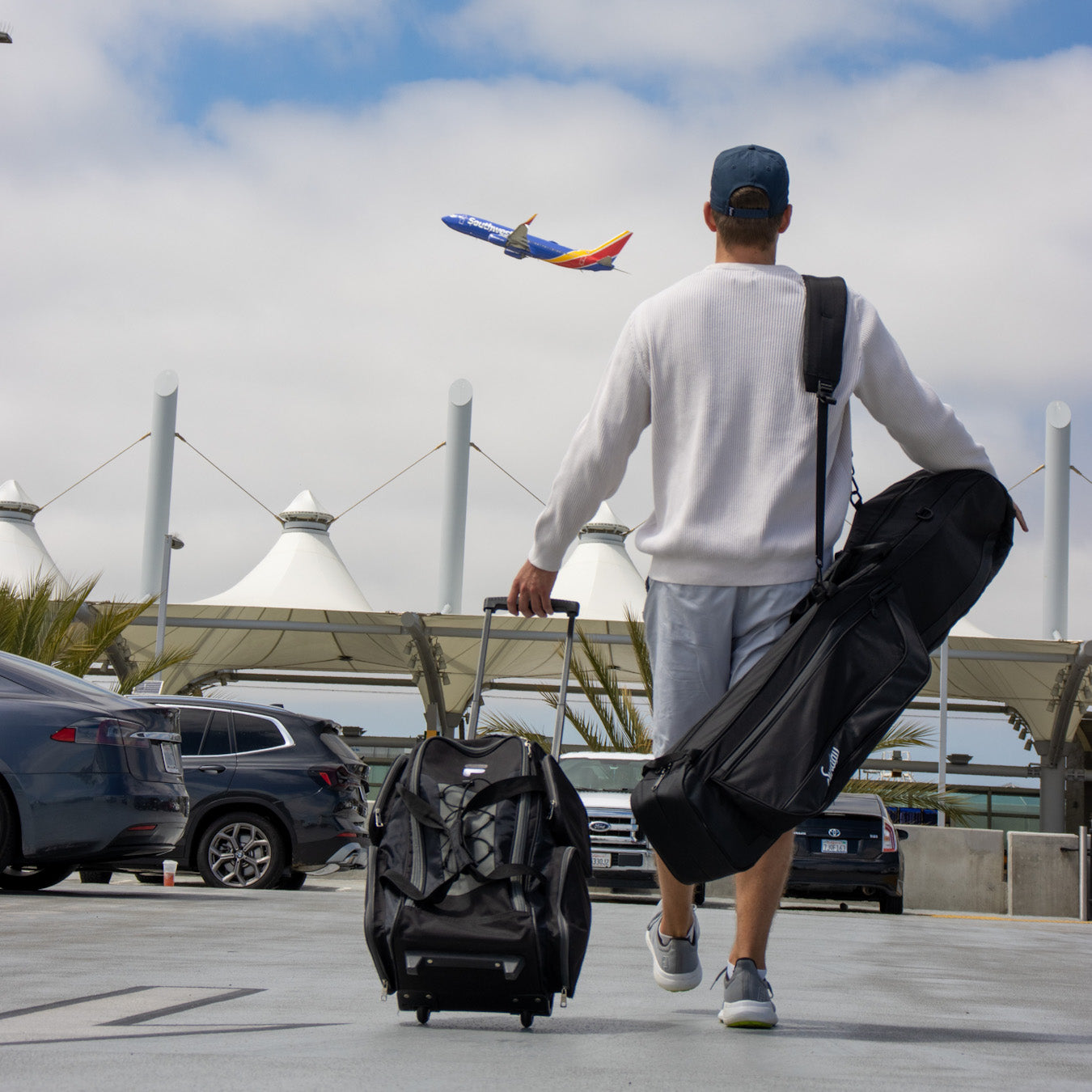 A man walking in the airport with a suitcase and the Mule travel golf bag on his back