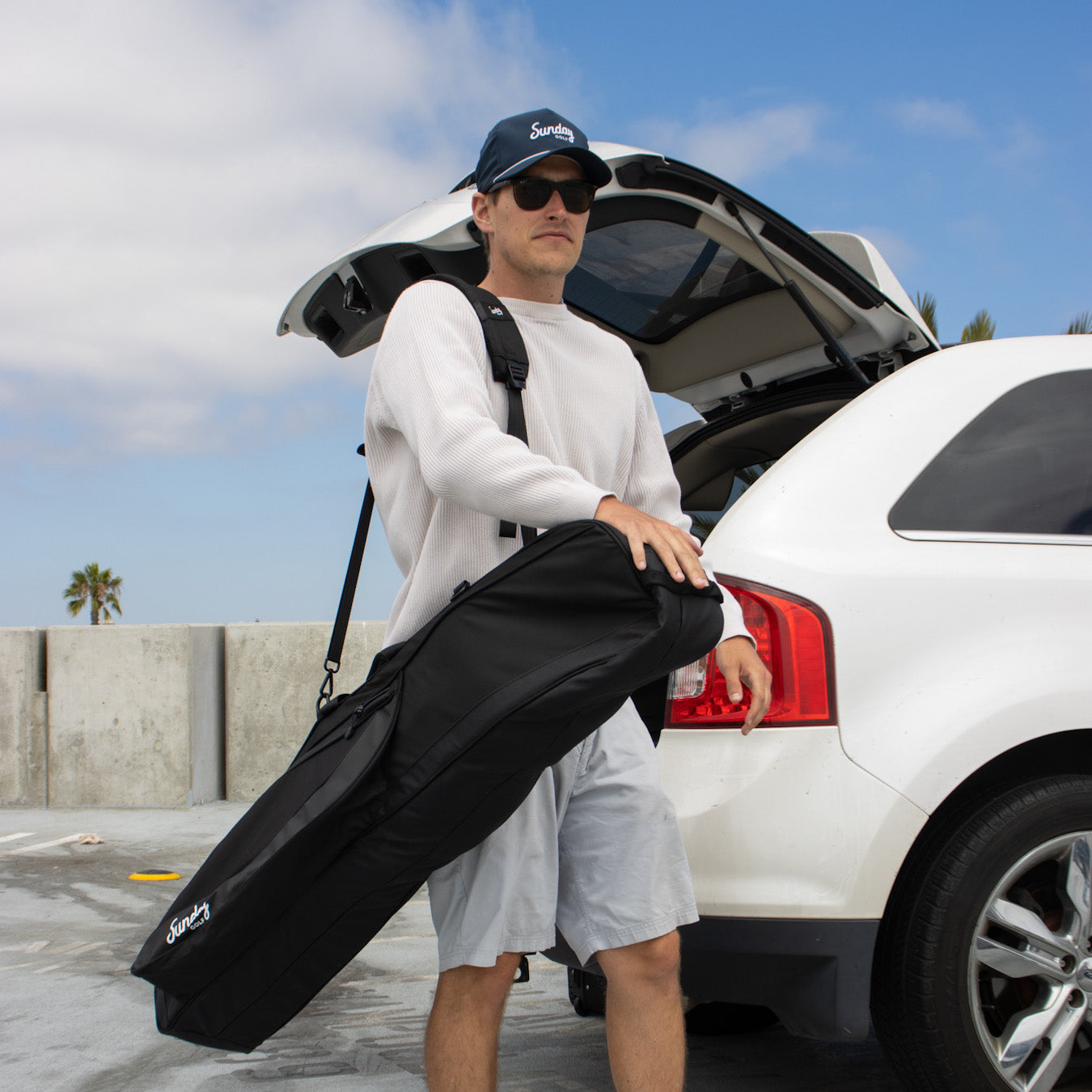 A man wearing a Sunday Golf rope hat and carrying a Mule travel golf bag
