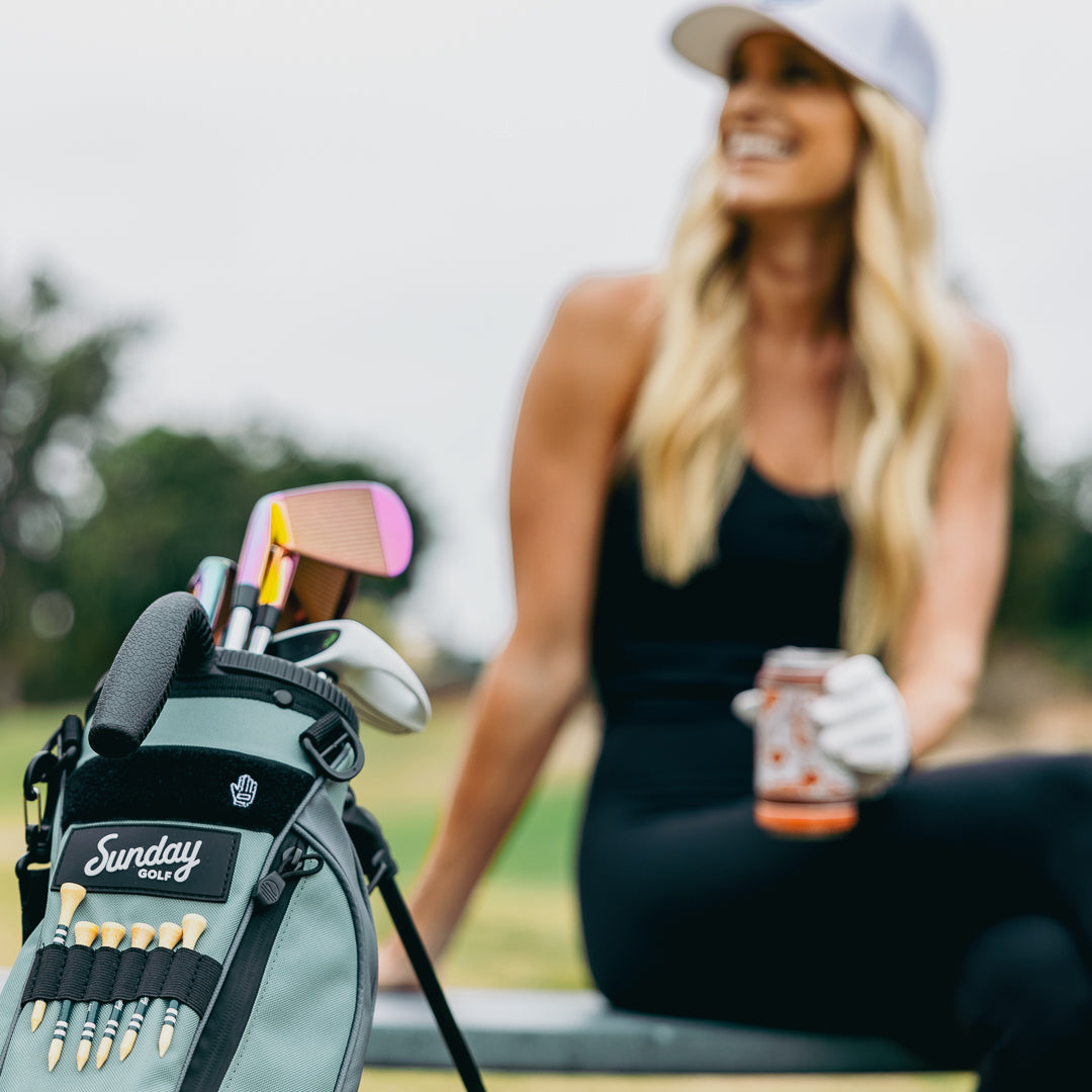 Seafoam Loma golf bag with tees, clubs, and a woman smiling in the background 